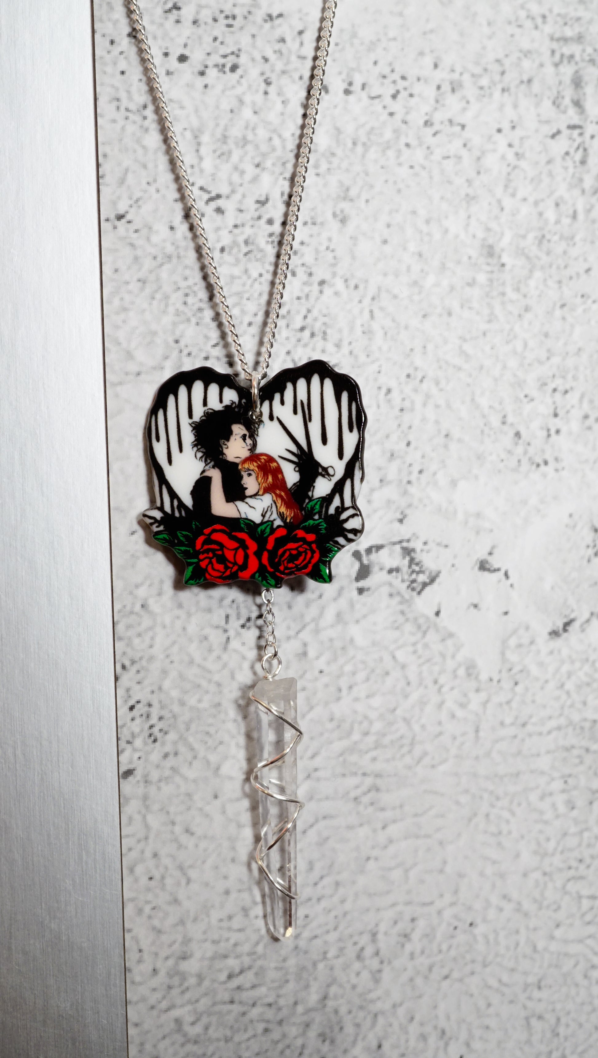 Necklace with a heart-shaped pendant featuring a edward scissor hands and kim. Red roses on  textured white heart with black drops. snowy white background
