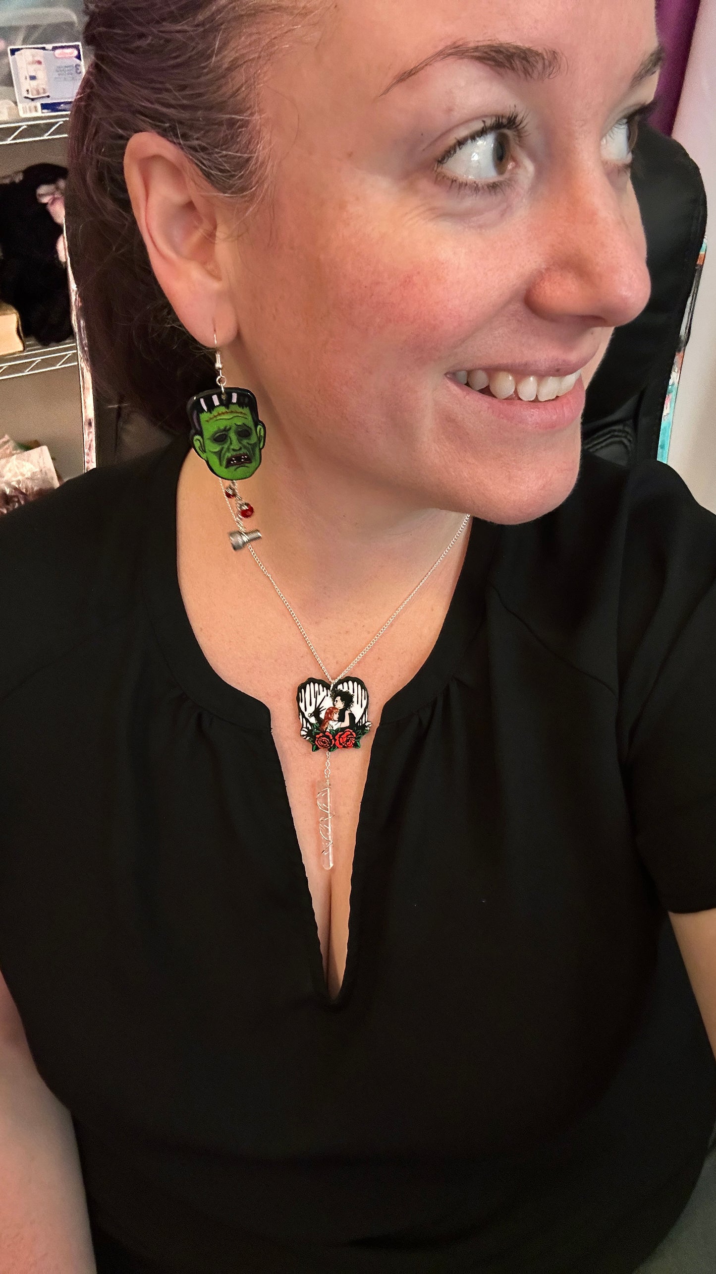 woman wearing creepmas jewelry. frankenstein's monster earrings with steel bolts, and edward scissorhands heart necklace with clear quartz. wearing black shirt. 