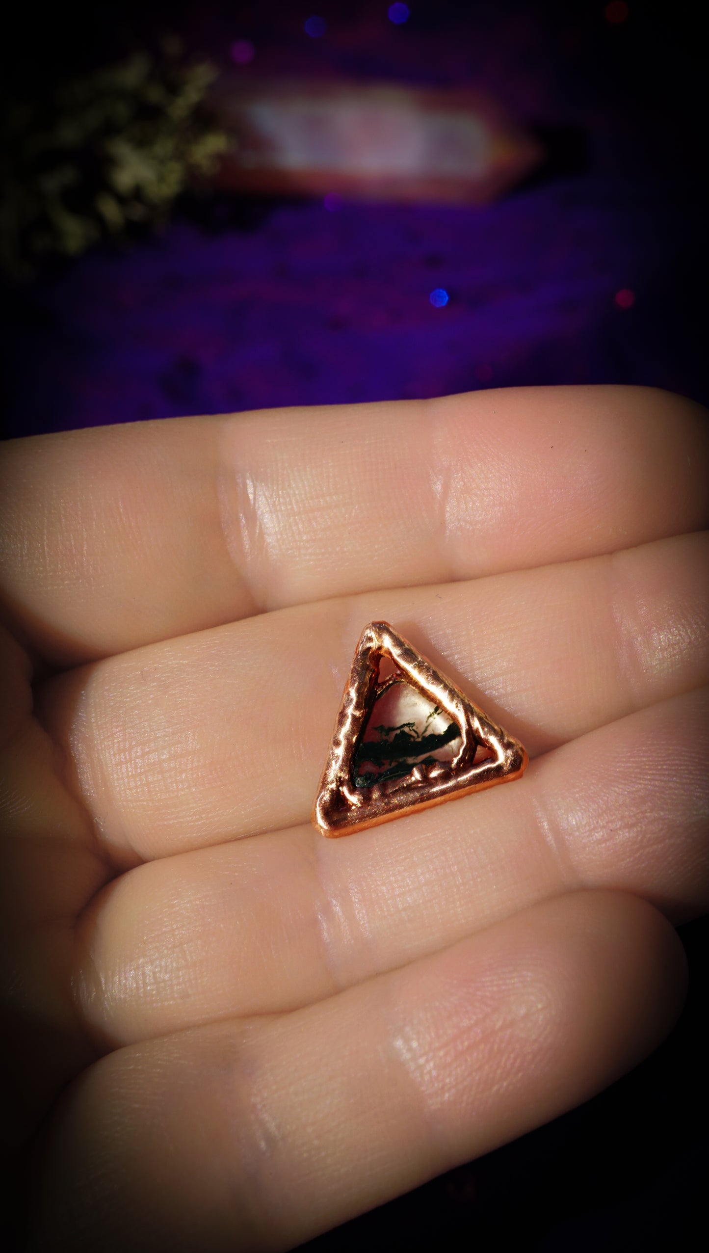 light copper triangle with dark green moss gate in center, in hands, with purple background
