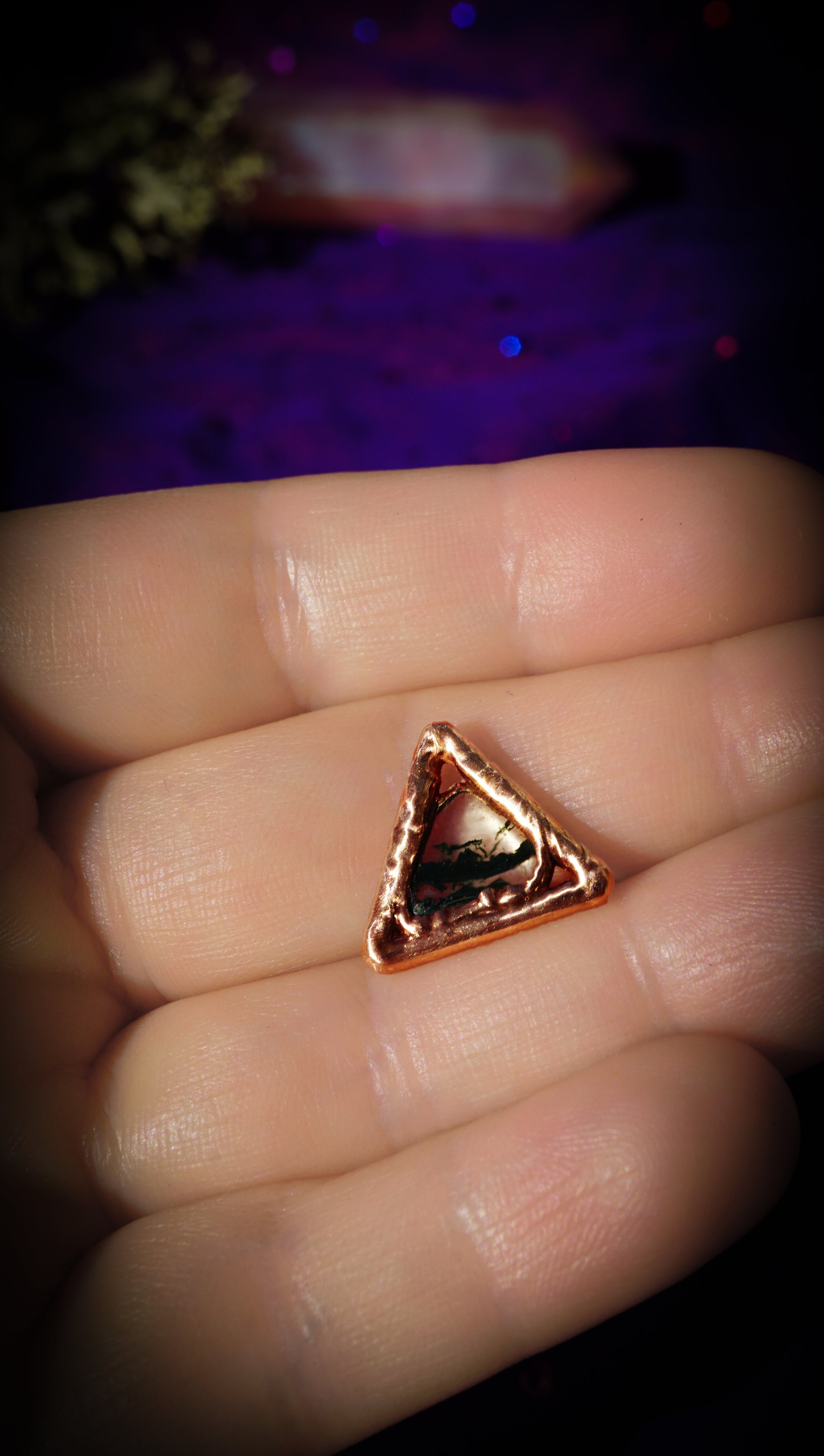 light copper triangle with dark green moss gate in center, in hands, with purple background