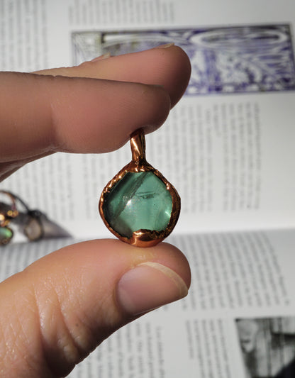 light Green gemstone pendant with copper setting held between fingers against an old book