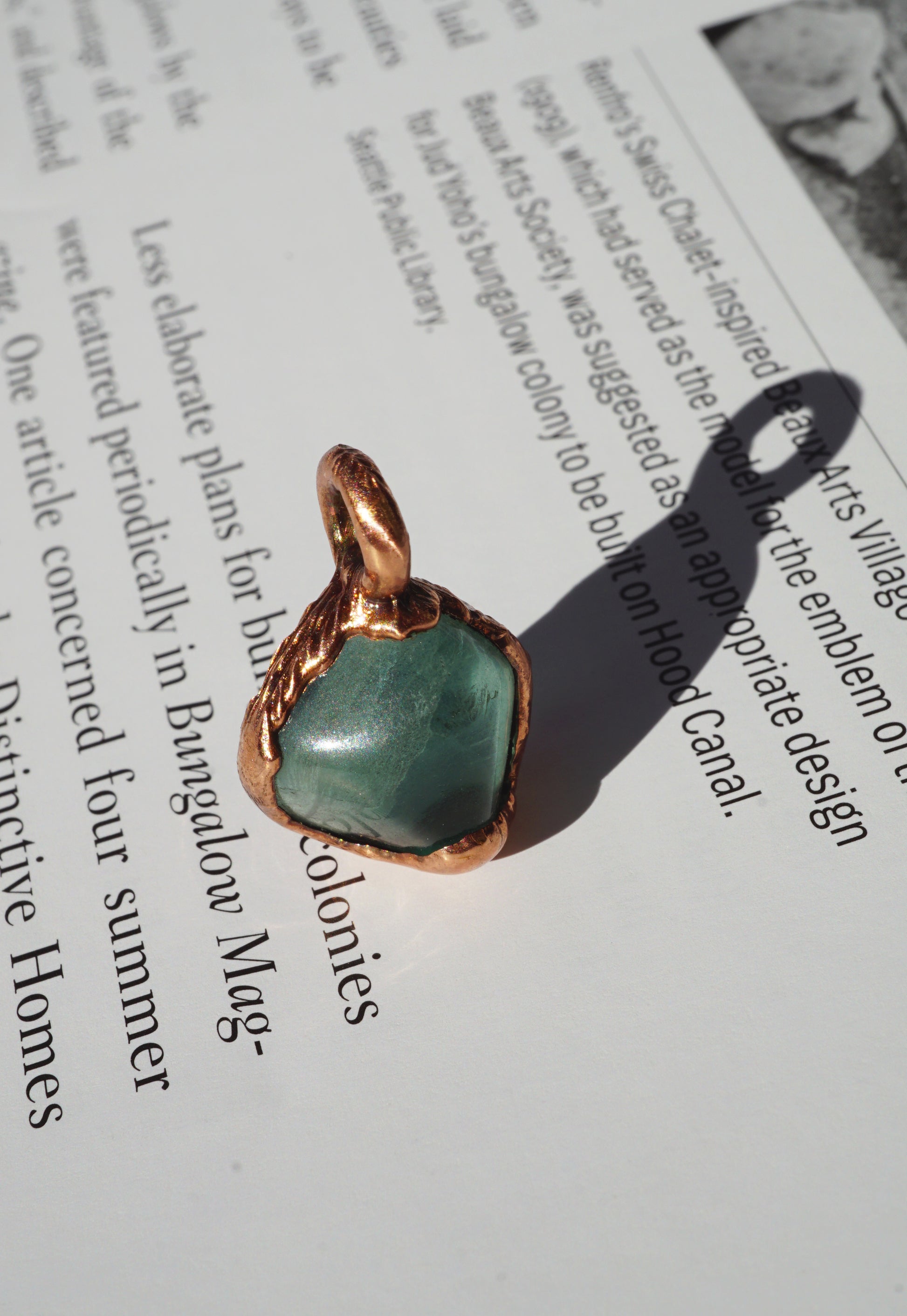 soft green stone in medium toned copper setting, against book page with shadow from pendant
