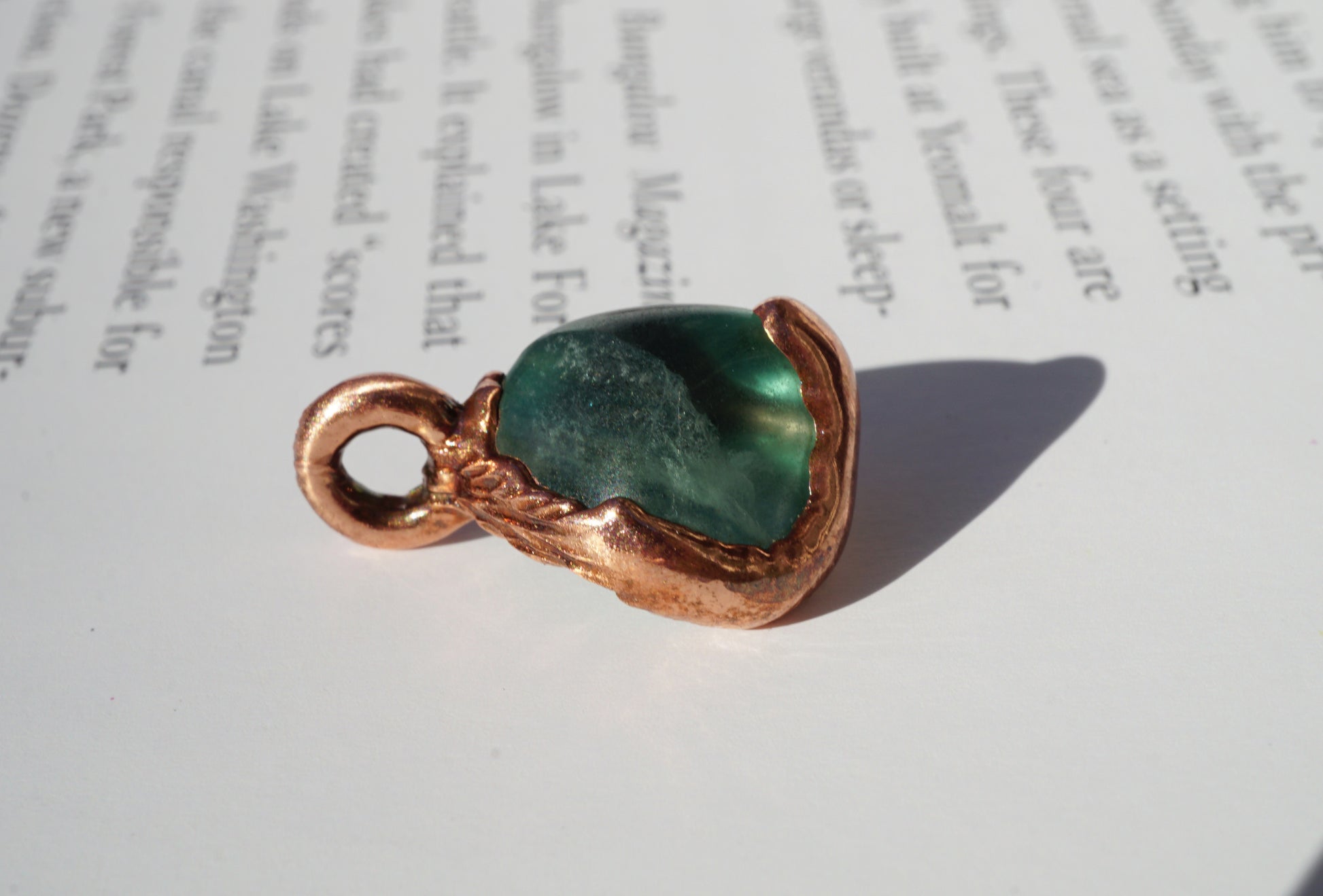 soft green stone in medium toned copper setting, against book page
