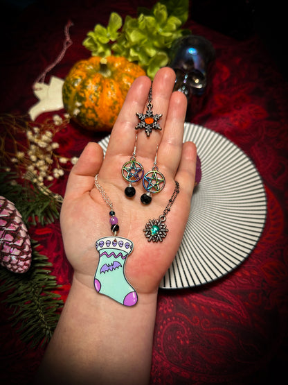 jack o lantern snowflake necklace, green skull snowflake necklace, rainbow anodized metal pentacle & black crystal witch earrings, and a beaded necklace with a light blue stocking that has a cute little pink bat
