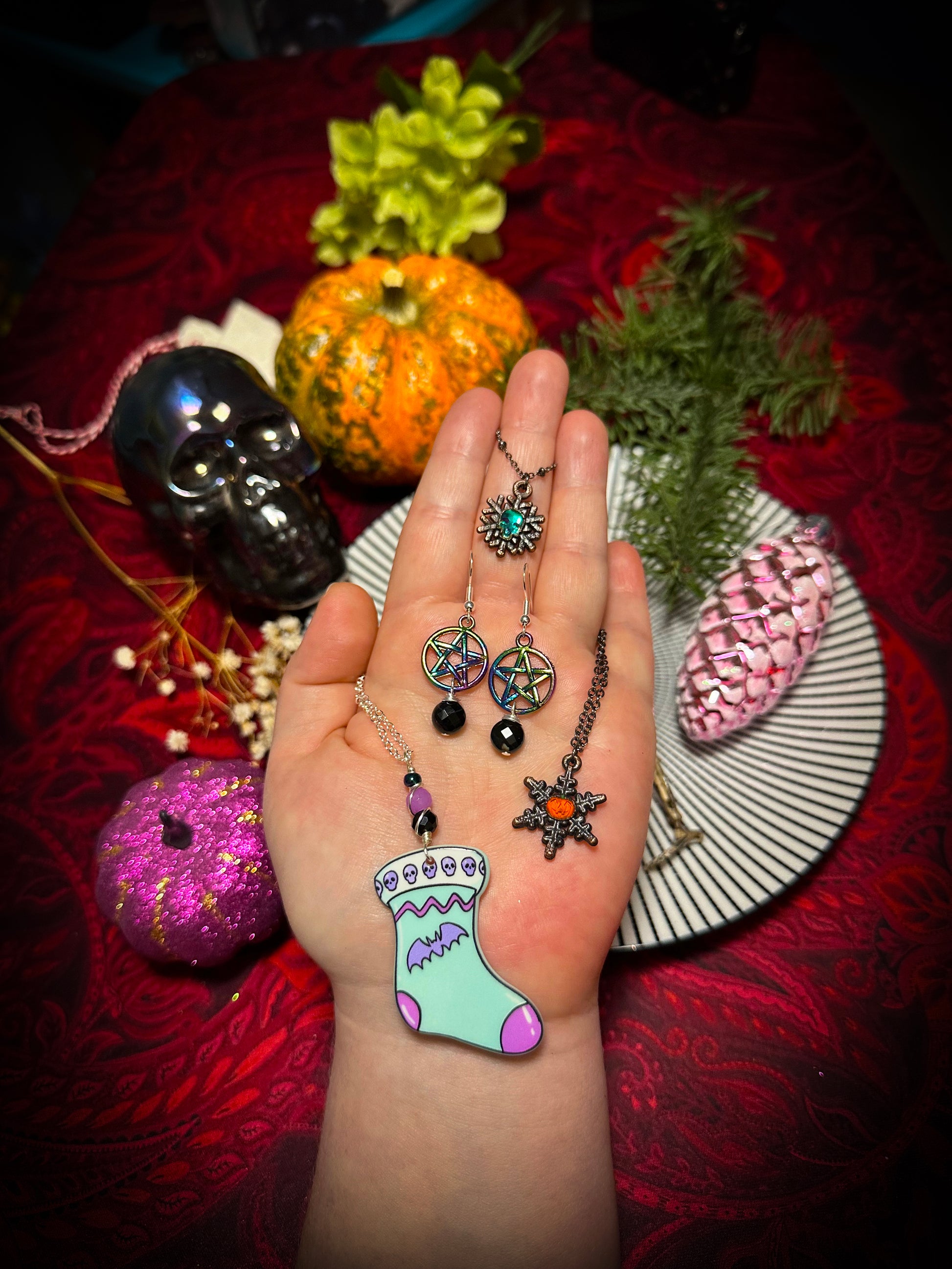 gothic spookmas jewelry in my hand for reference with spooky pumpkins and items behind it