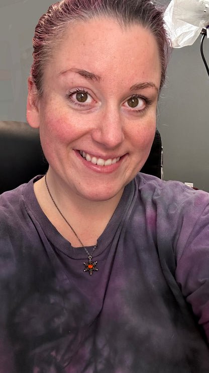 Person wearing a purple shirt with a jack o lantern snowflake necklace. sitting in an office chair.